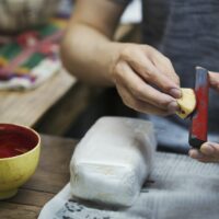 Close up of woman working in a Japanese porcelain workshop, holding red paint stick and sponge.