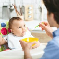 Hungry baby eating healthy kid food in kitchen