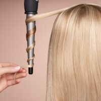 The hairdresser curls long hair with a Curling iron