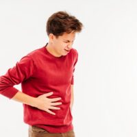 Young man holding liver, experiencing pain on white background